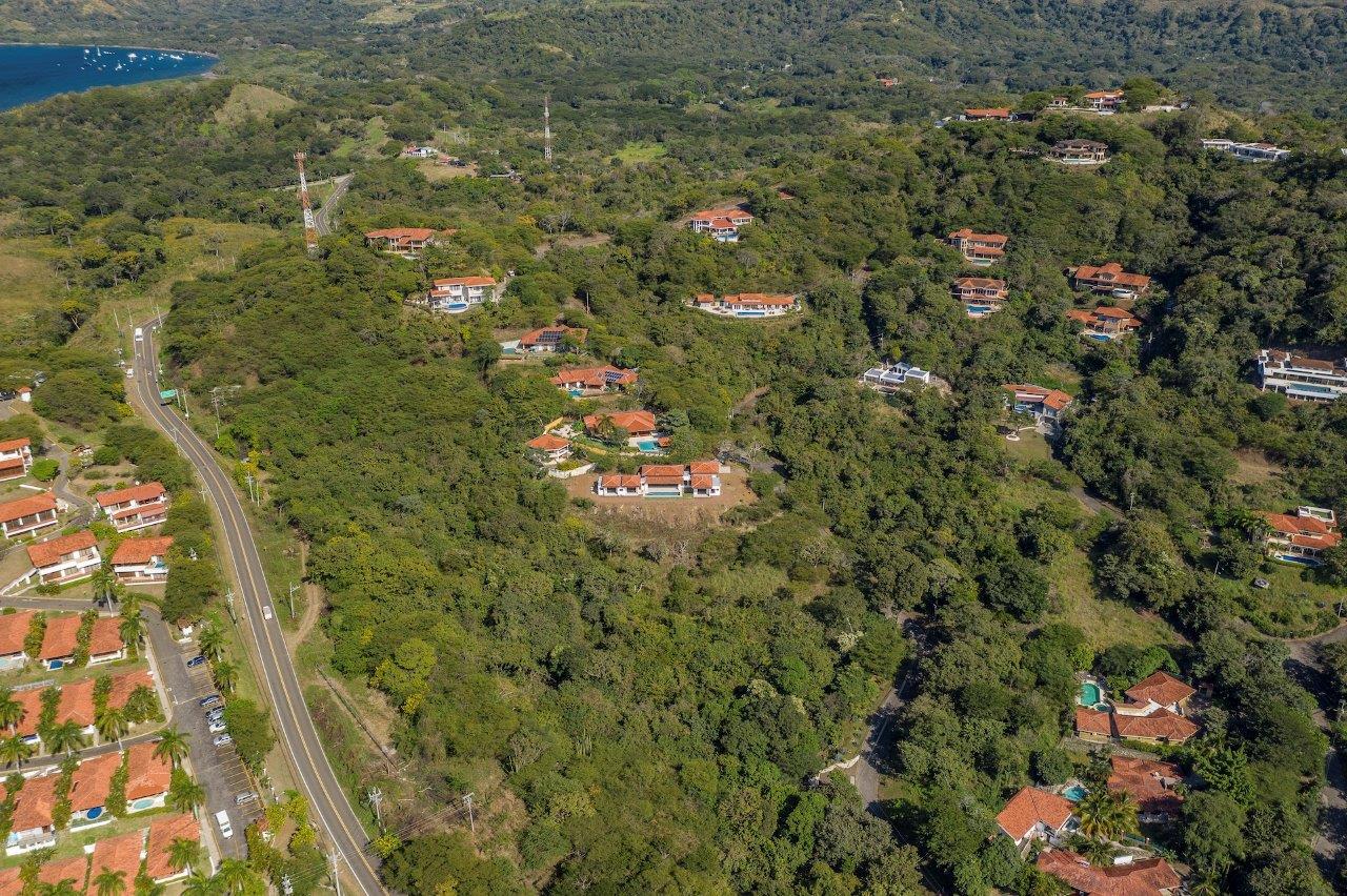 Aerial view of a hillside residential development surrounded by dense tropical forest, with modern homes, winding roads, and ocean glimpses in the distance, representing hillside living opportunities in the Costa Rica real estate market.